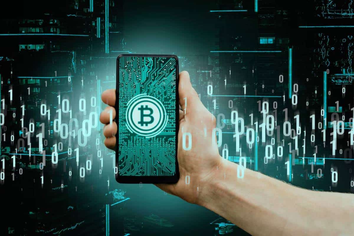 Hand holding a smartphone displaying a Bitcoin logo over a circuit board, against a digital data background.
