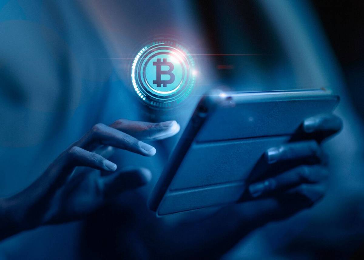 Person using a tablet with a glowing Bitcoin symbol visible, suggesting cryptocurrency interaction.