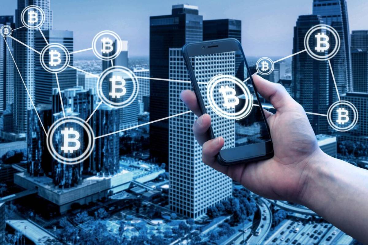 Hand holding smartphone with Bitcoin symbols connecting to a cityscape, illustrating cryptocurrency and blockchain concept.