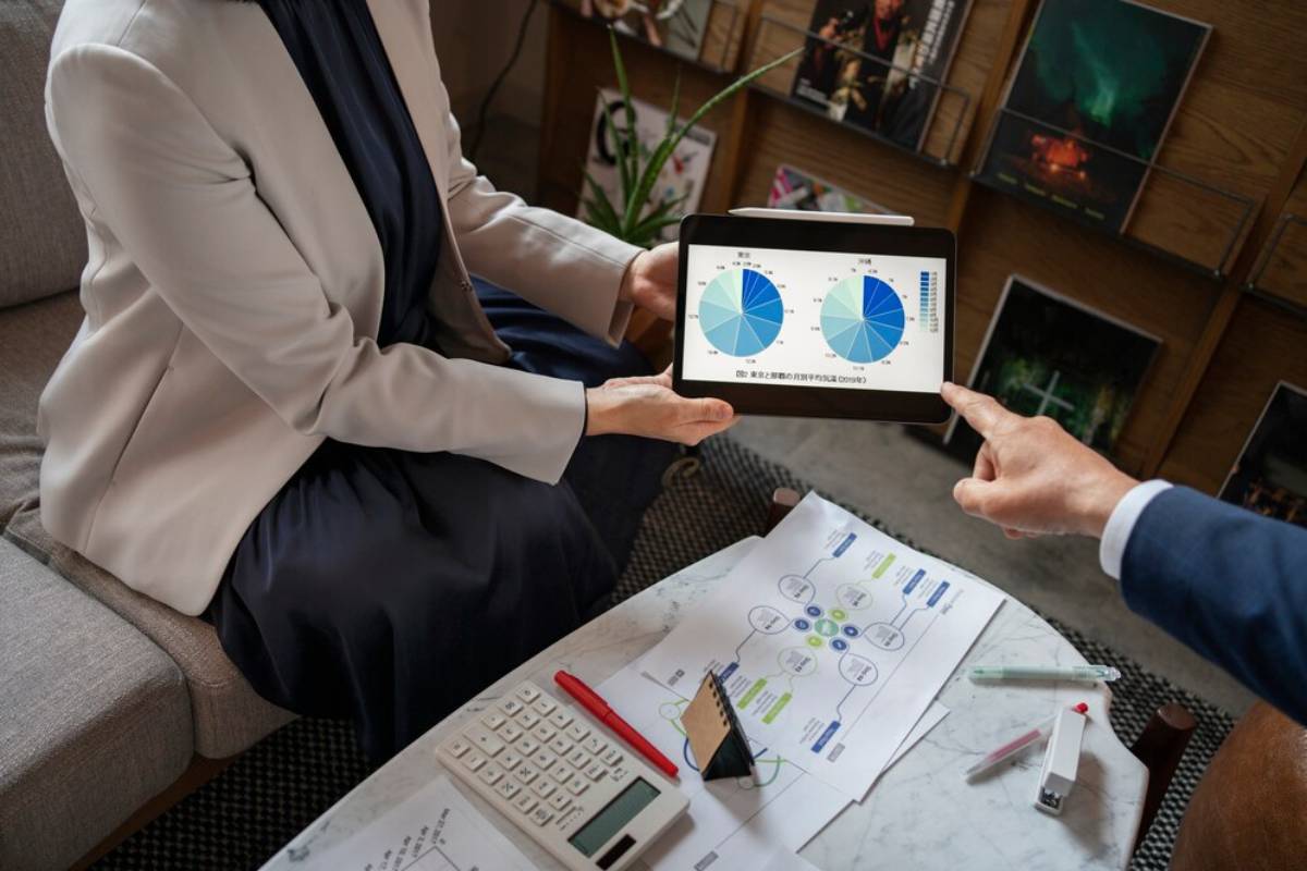 Two professionals analyzing pie charts on a tablet in an office setting.