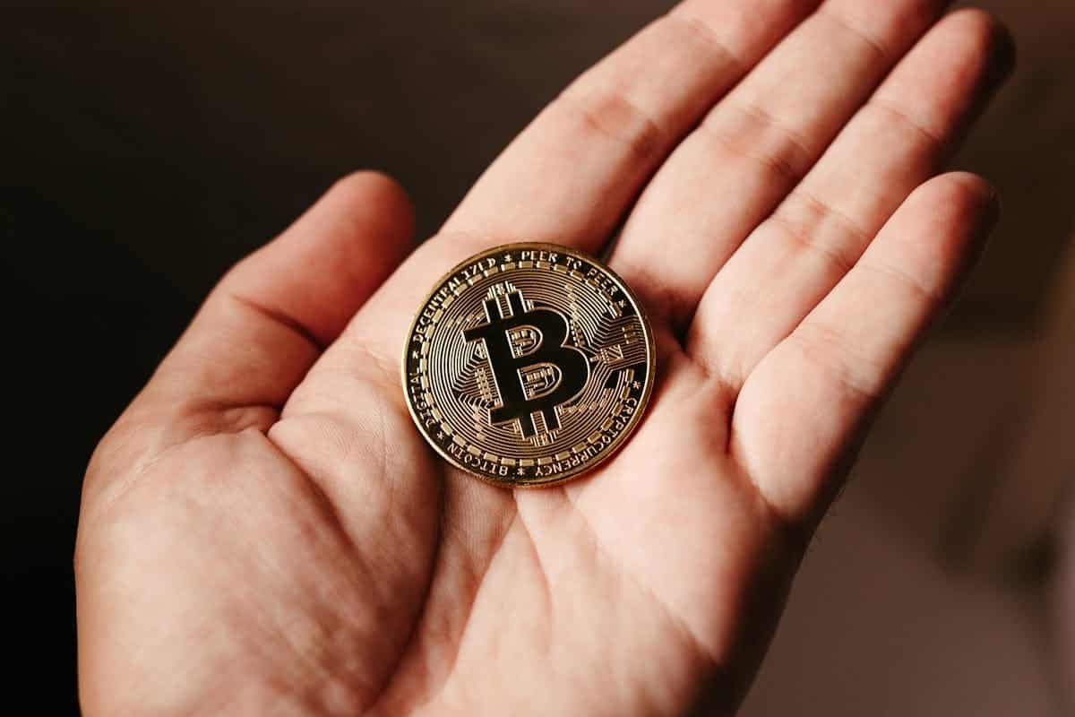 A person holding a shiny Bitcoin token in their open hand.