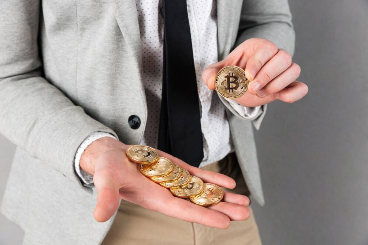 A man in a business casual outfit holding several Bitcoin tokens in his hand.
