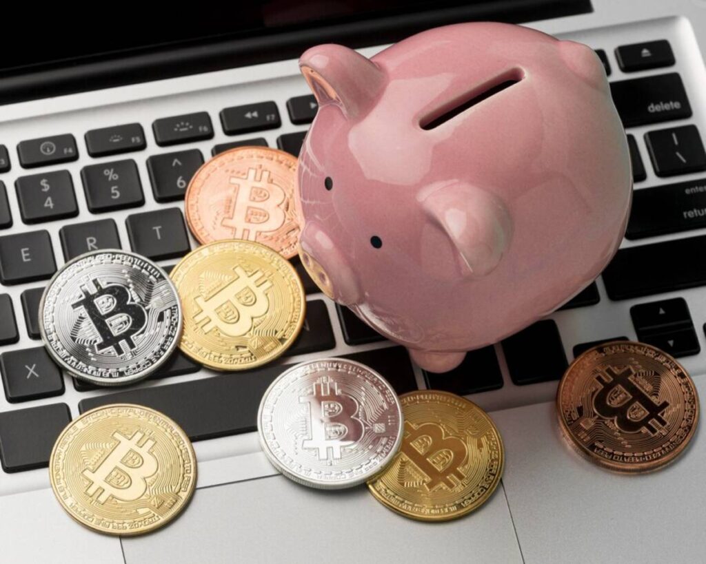 A pink piggy bank on a laptop keyboard surrounded by various Bitcoin coins.
