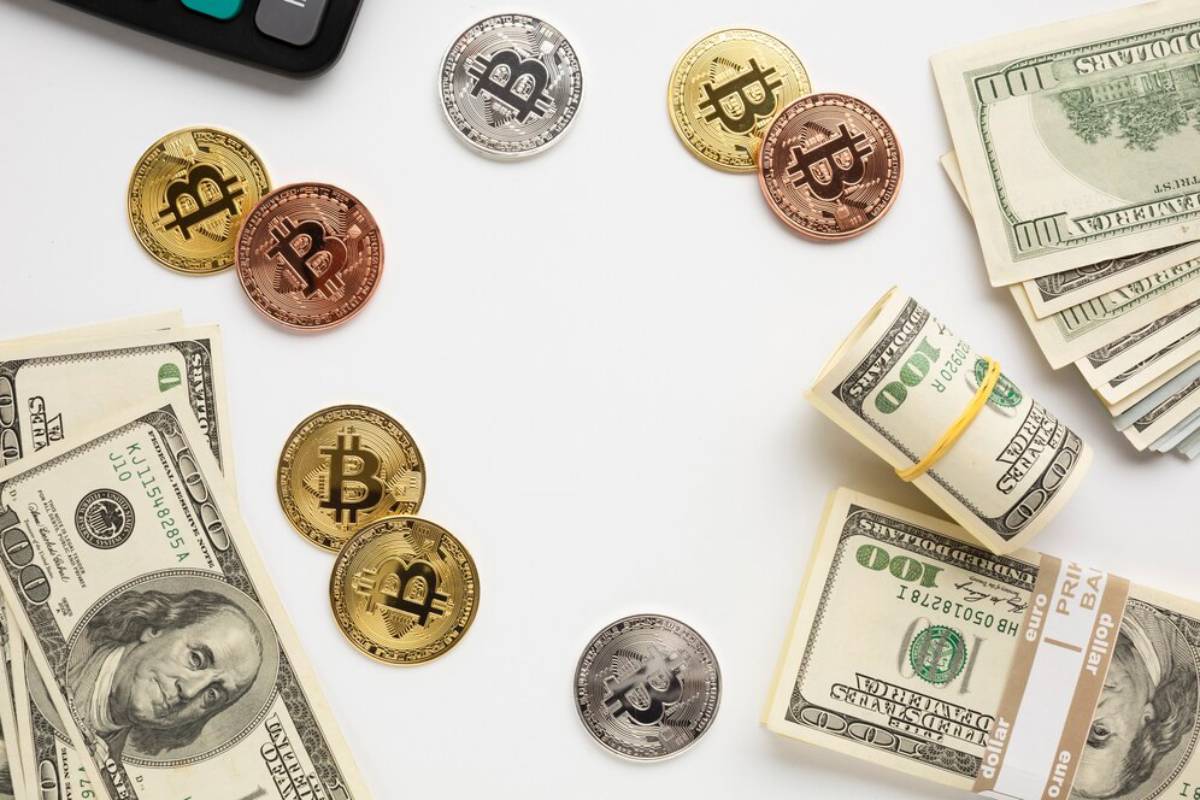 Various Bitcoin tokens scattered with U.S. dollar bills on a white background.
