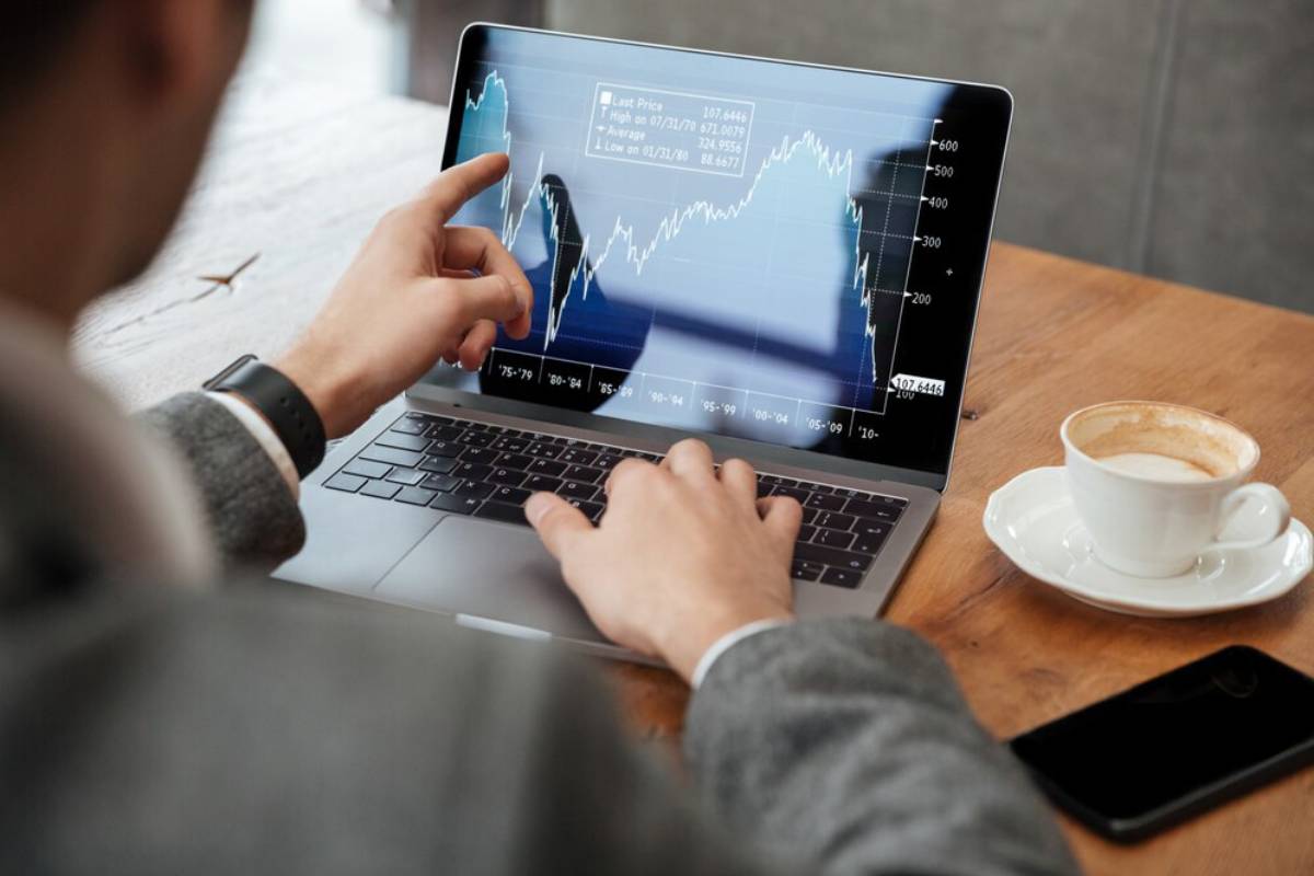 Person analyzing financial graphs on a laptop screen, with a coffee cup and smartphone on the table.