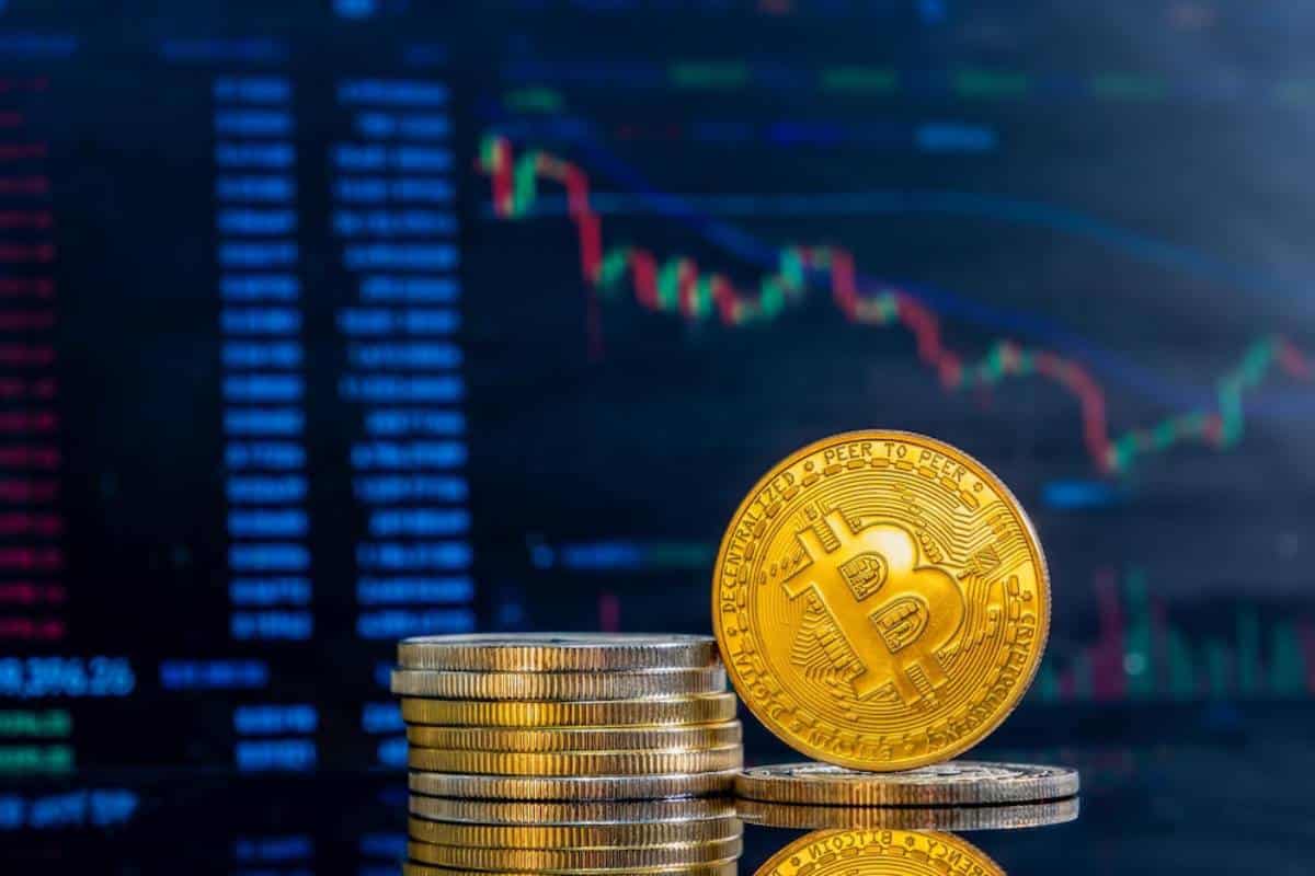 Bitcoin gold coin stacked with blurred cryptocurrency trading data in the background.