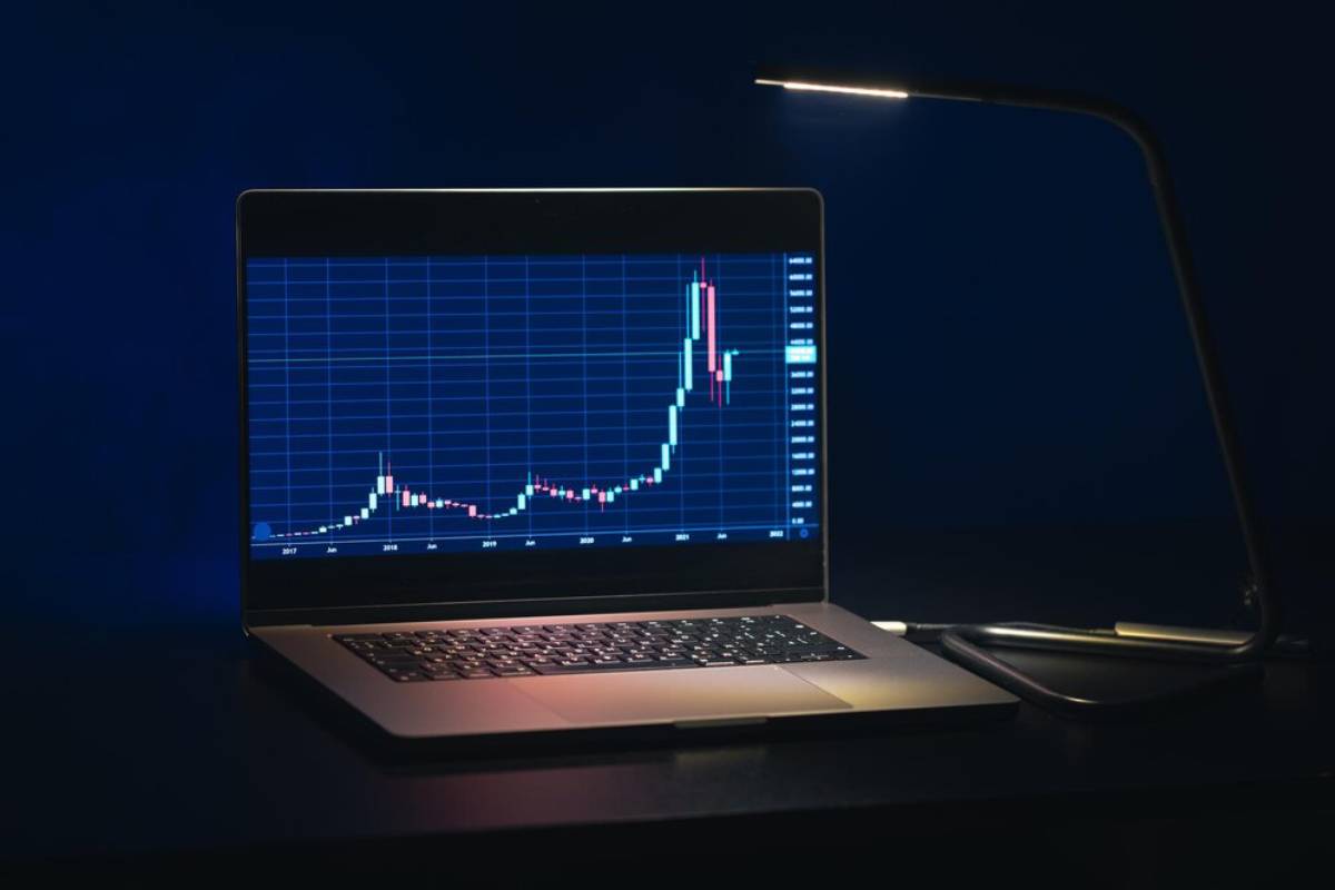 Laptop displaying a stock market chart under a lamp with a dark blue background.