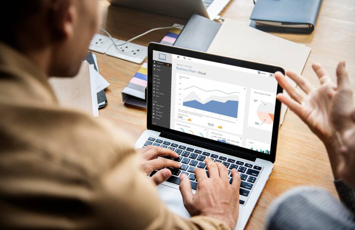 Two people discussing business data on a laptop screen in an office setting.