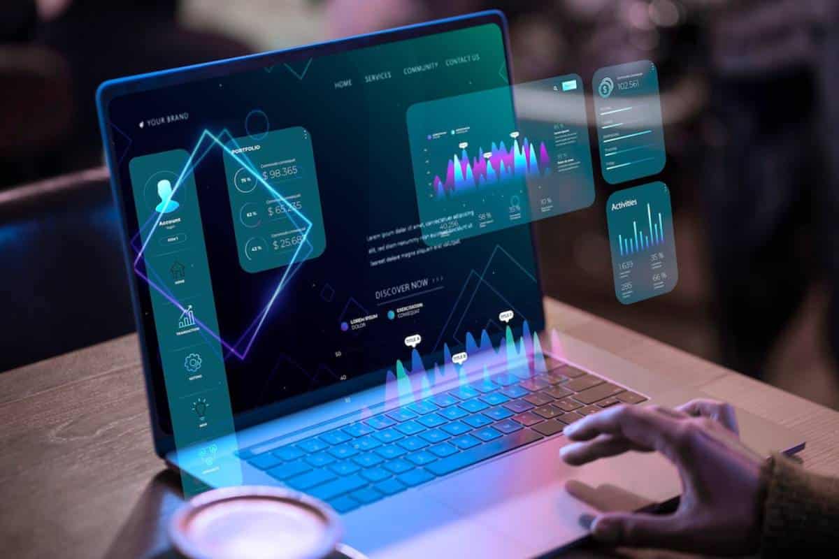 Person interacting with futuristic holographic analytics displayed on a laptop screen in a dimly lit setting.