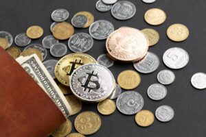 Various international coins, a few banknotes, and cryptocurrency tokens including Bitcoin, on a dark background.