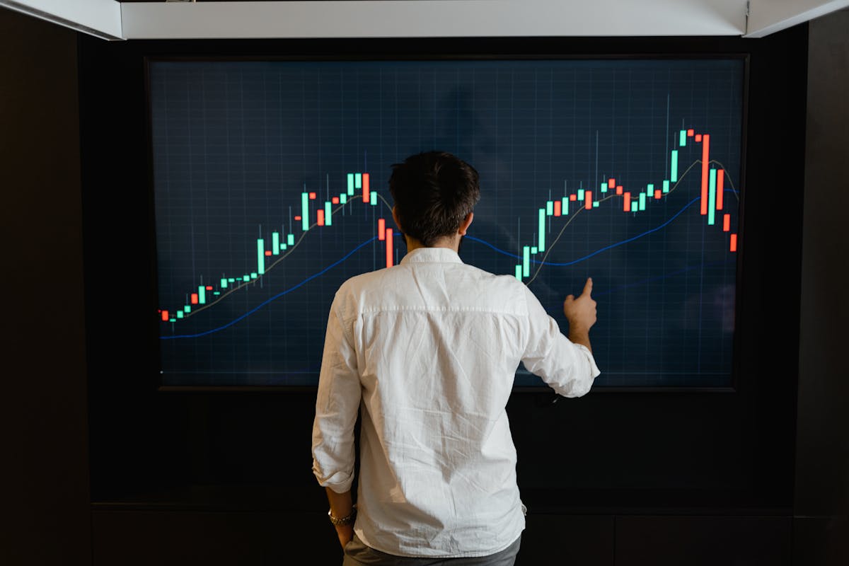 Man in white shirt analyzing stock market trends on a large digital screen.