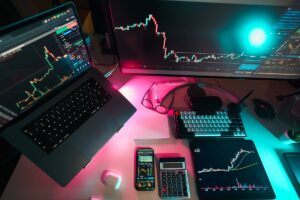 Workspace showing multiple screens with stock market graphs, lit by neon lights.