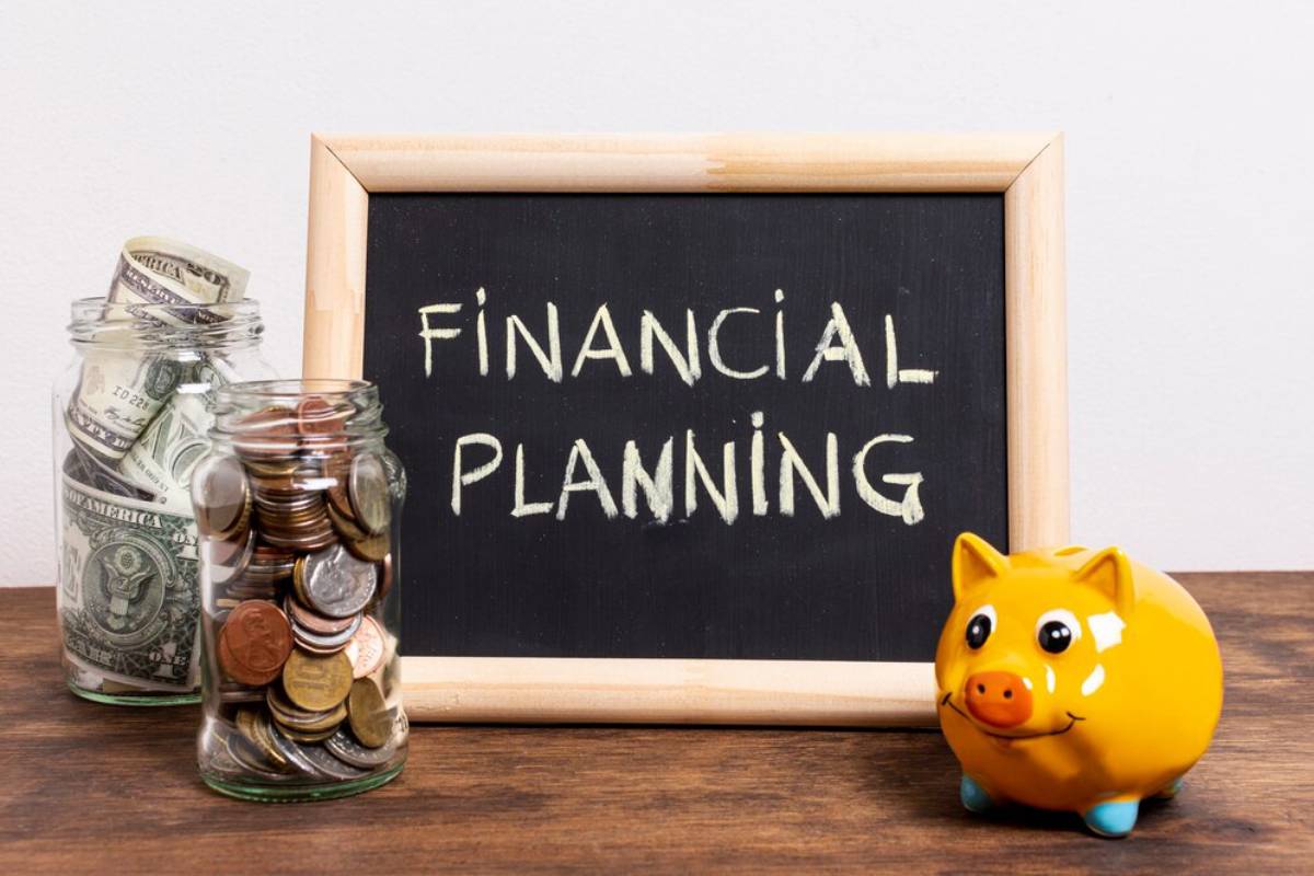 A chalkboard reading FINANCIAL PLANNING with jars of money and a piggy bank on a table.