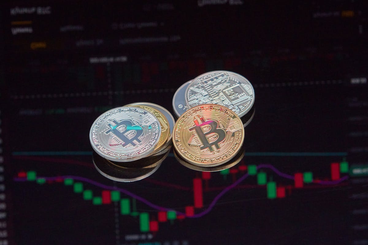 Three Bitcoin coins stacked with financial graph background showing market trends.