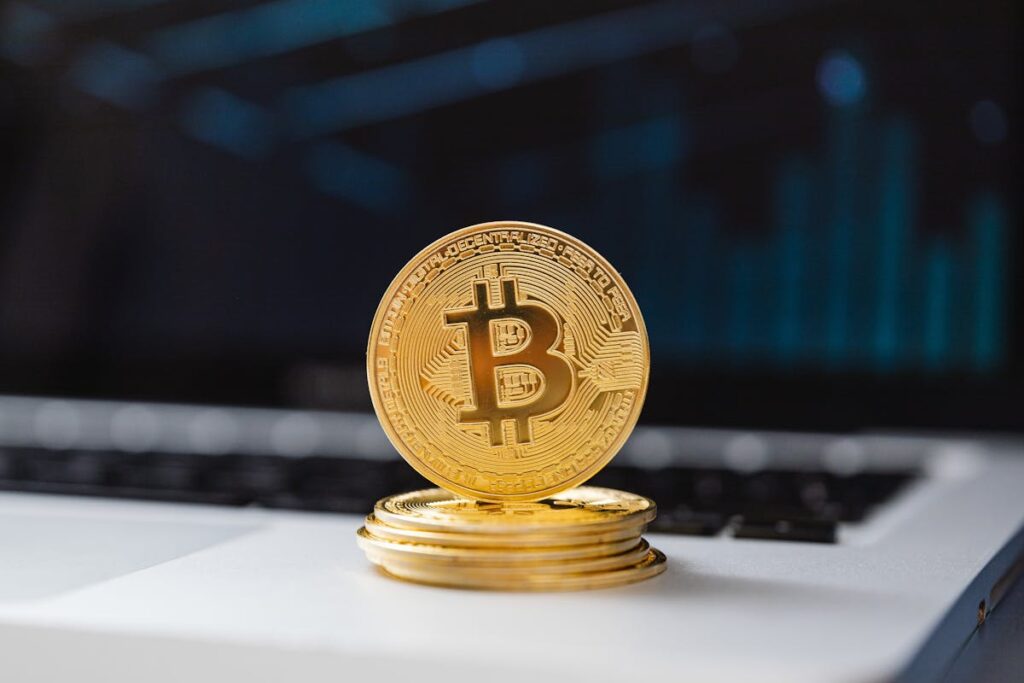 Stack of Bitcoin coins on a laptop keyboard with a blue data chart in the background.