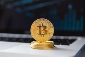 Stack of Bitcoin coins on a laptop keyboard with a blue data chart in the background.