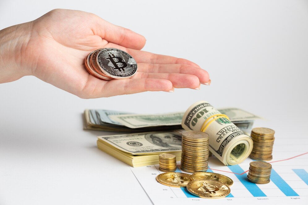 Hand holding Bitcoin over a background of U.S. dollars, coins, and financial charts.