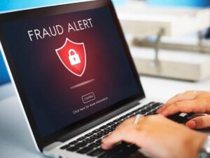 Laptop screen displaying a Fraud Alert" message with a lock icon, while a person's hands are typing on the keyboard.
