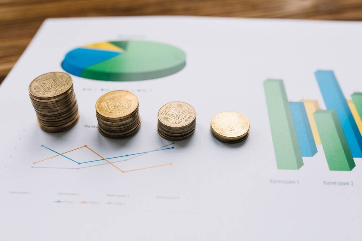 Stacks of coins placed next to colorful pie and bar charts on a financial report, representing data analysis