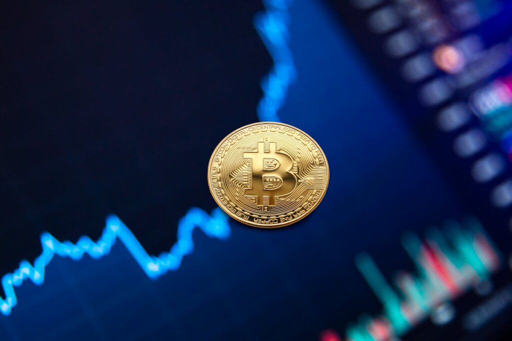 A gold Bitcoin coin suspended in mid-air against a blurred background of colorful stock market graphs.