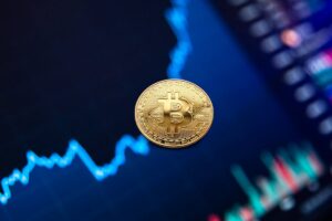 A gold Bitcoin coin suspended in mid-air against a blurred background of colorful stock market graphs.