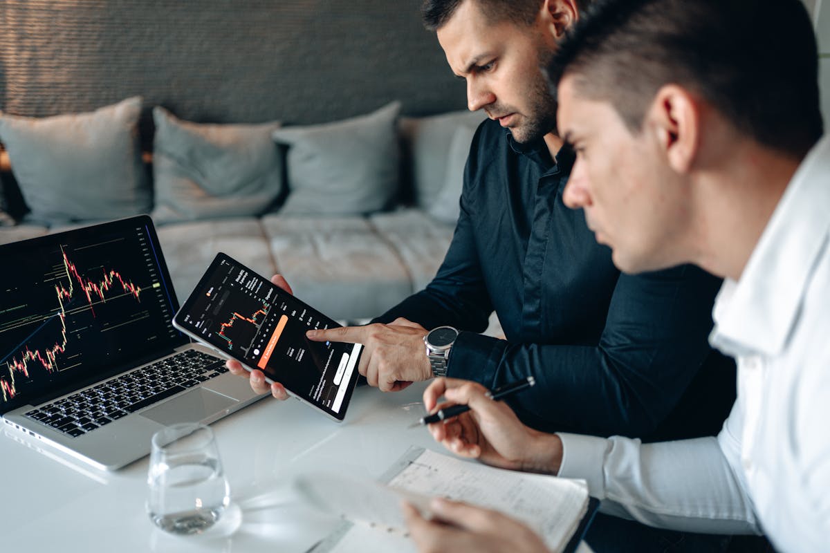 Two men analyzing financial data on a laptop and tablet in a modern office setting.