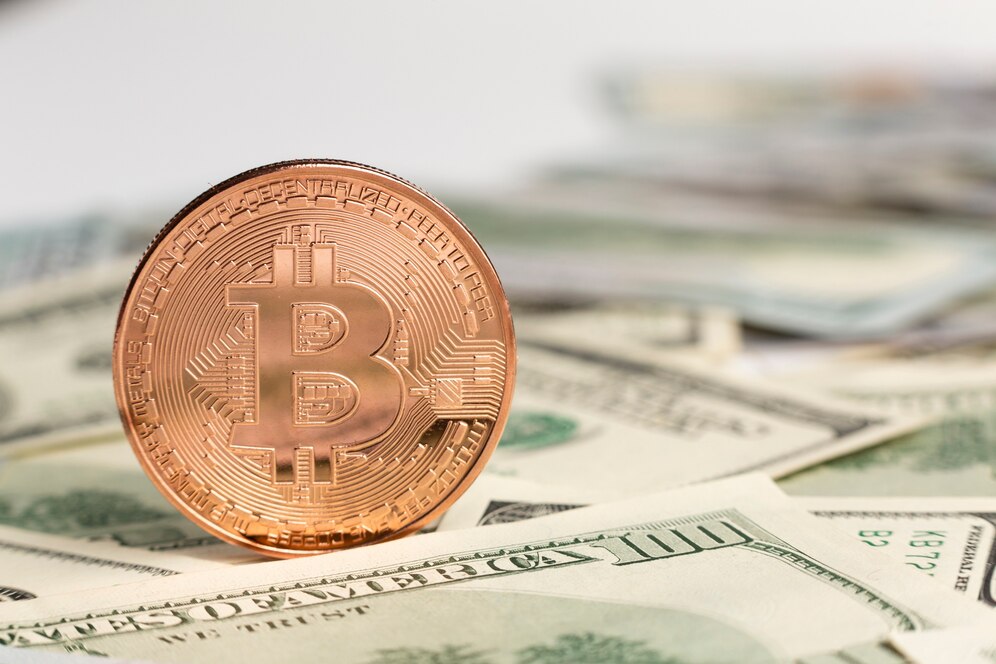 A bronze Bitcoin coin stands upright on a background of scattered US dollars.