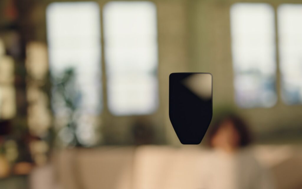 A blurred indoor scene with a silhouetted object in focus, while a person relaxes in the background, surrounded by natural light.