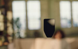 A blurred indoor scene with a silhouetted object in focus, while a person relaxes in the background, surrounded by natural light.