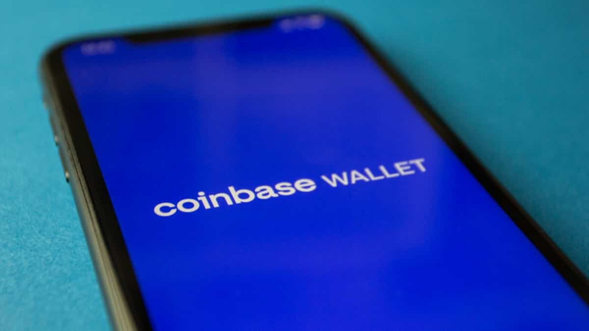 Close-up of a smartphone displaying the Coinbase Wallet app on a bright blue background. The app's name is clearly visible.